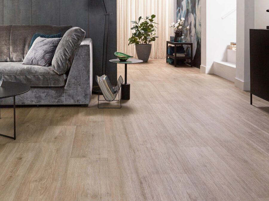 Woonkamer met vinylvloer in warme houtkleur, superzachte grijze bank en beige gordijnen.