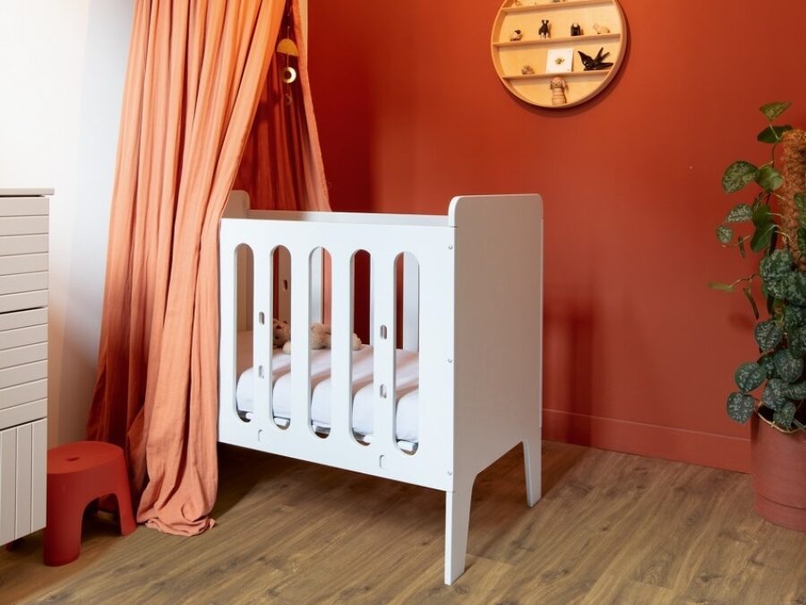 Babykamer voor meisje met wit ledikant, roze bedhemel, rode muur en laminaat vloer in warme kleur houtlook
