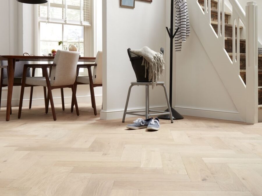 Eetkamer en hal in landelijke stijl met visgraat vloer en witte plinten weggewerkt rond trap en deurpost