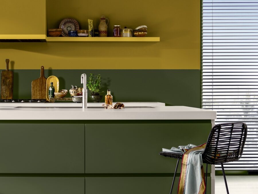 Keuken in Italiaanse stijl met muur in True Joy geel, mosgroene keukenkastjes en aardewerk kruidenpotjes als accessoires.