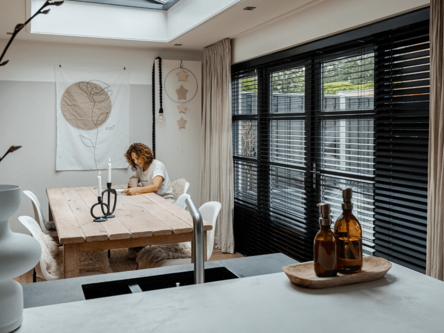 Vrouw in industriele keuken met zwarte jaloezieen en beige gordijnen