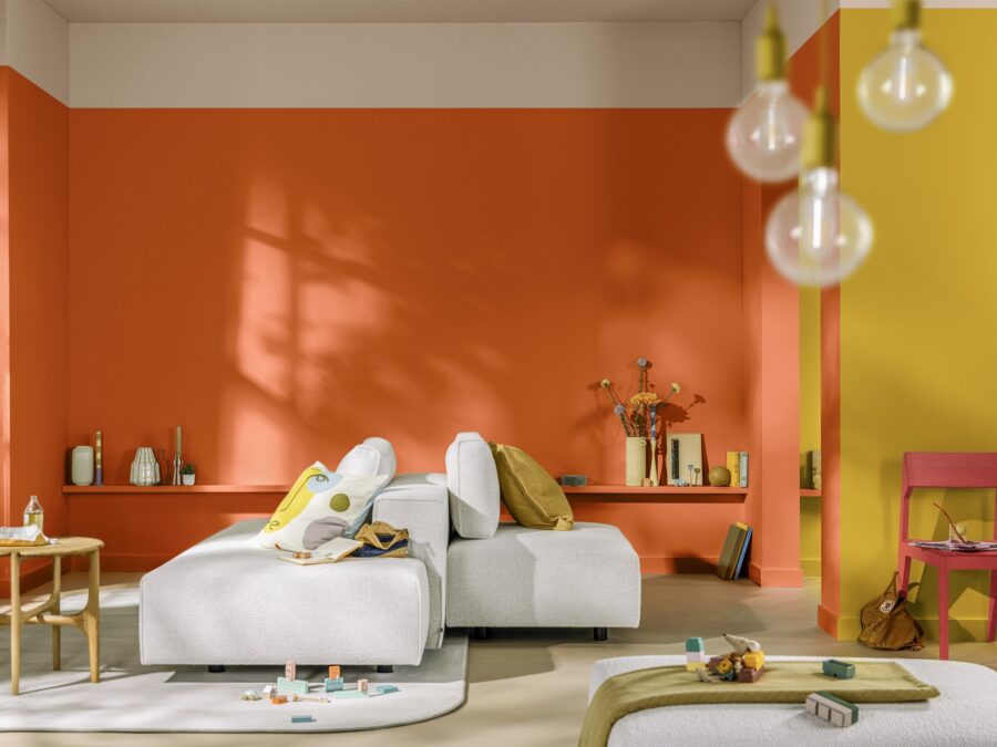 Woonkamer met beige loungebank, ovaal vloerkleed en warme tint muurverf in koraal en oker.