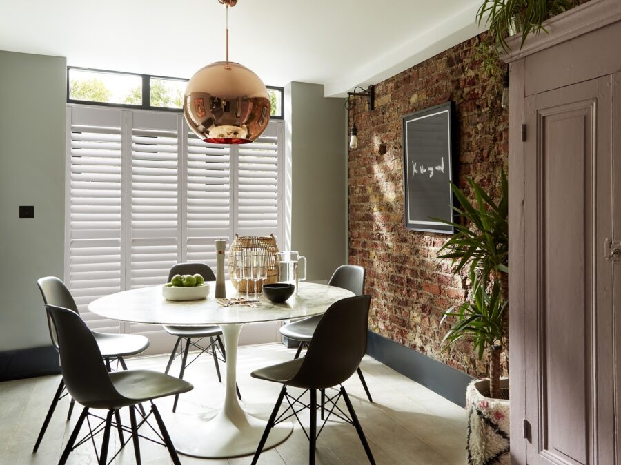 Eetkamer met witte houten shutters voor breed raam.