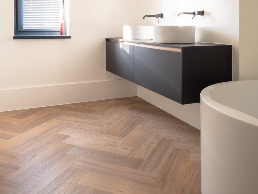 Badkamer met visgraat pvc vloer en hoge witte plint onder wastafel