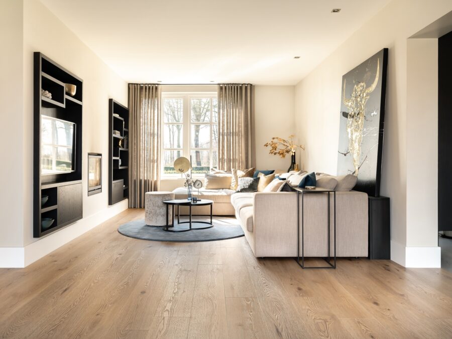 PVC-vloer met natuurlijke houttint in woonkamer met zwart wandmeubel en transparante gordijnen.