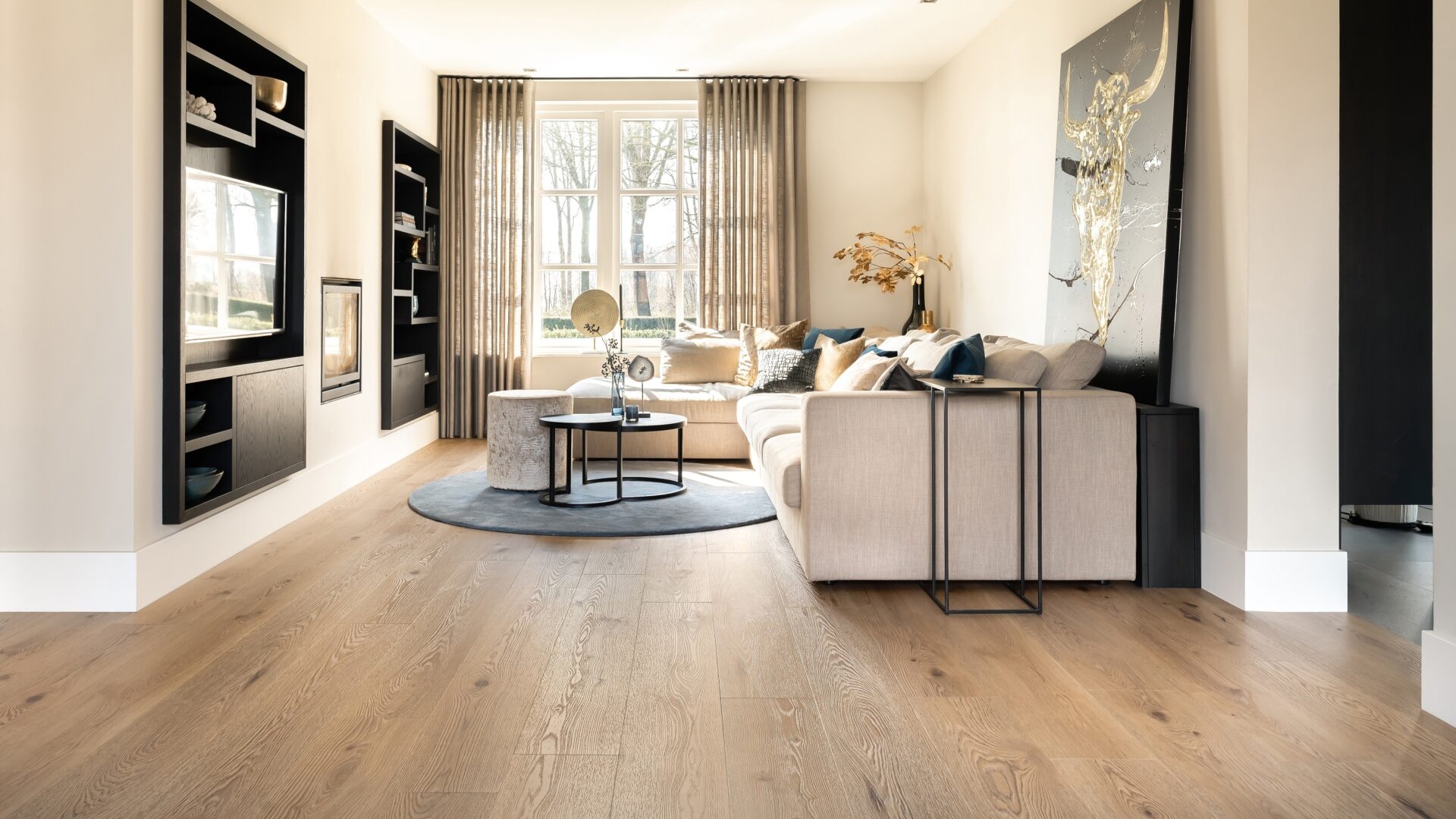 PVC-vloer met natuurlijke houttint in woonkamer met zwart wandmeubel en transparante gordijnen.