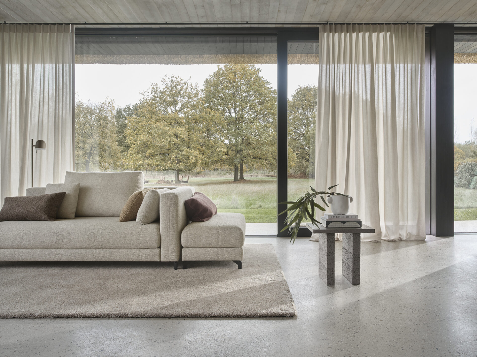 Woonkamer met witte gordijnen voor schuifpui, passend bij een relax bank en zacht vloerkleed.