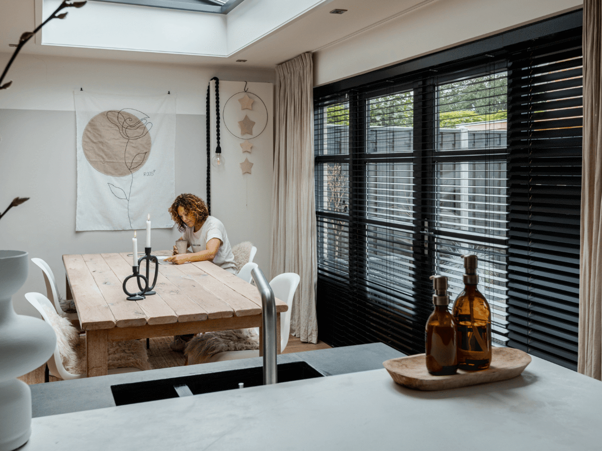 Vrouw in industriele keuken met zwarte jaloezieen en beige gordijnen