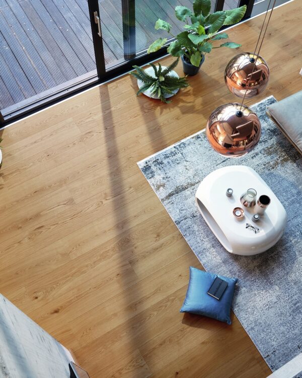 Ruime woonkamer moderne stijl met grijze loungebank, koperen lampen en laminaat in een warme bruintint.