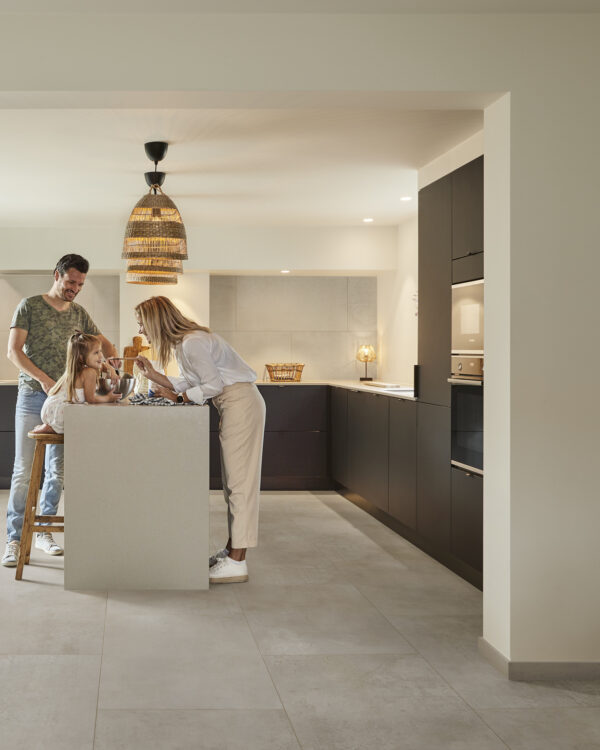 Keuken met grote pvc-vloer tegels in lichtgrijs, zwarte keukenkasten, keukenblok met gezin en sfeerverlichting.