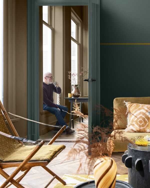 Woonkamer met muren in warme beige en turkoise tinten, houten vloer en gezellige bank, passend bij de botanische woonstijl.