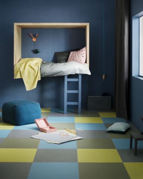 Kinderkamer met blauwe wand, bedstee en vloer van marmoleum tegels in speelse kleuren geel, blauw en grijs.