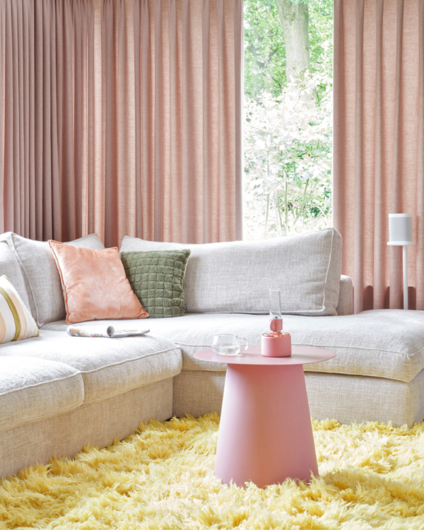 Roze inbetween gordijnen voor in de woonkamer met een grijze bank en een geel vloerkleed