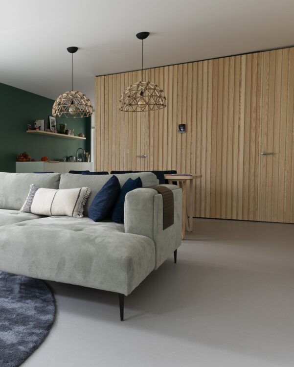 Woonkamer met lichtgrijze marmoleum vloer, grote hoekbank en wandpanelen in eikenhout look.