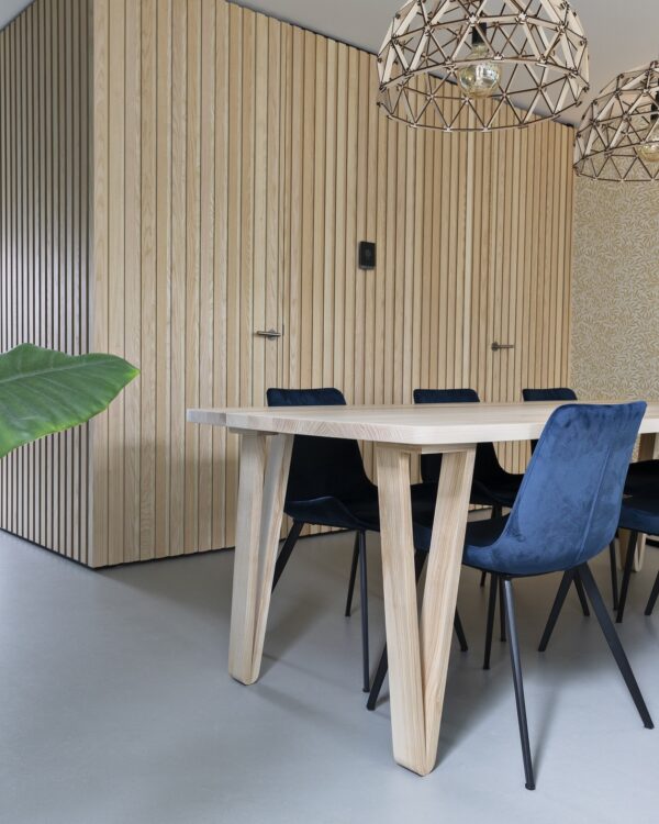 Eetkamer met grijze betonlook marmoleum vloer, houten tafel, stoelen met metalen poten en houten wandpanelen aan de muur