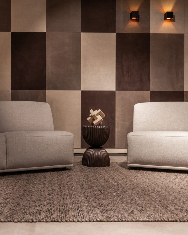 Woonkamer met leren wandbekleding van Belledo in bruin en beige tinten met grijze 2 zits en fauteuil.