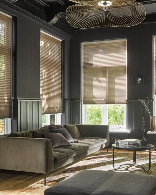Woonkamer met grote ramen, 3zits bank, muren met warme grijstint muurverf en plissés van Luxaflex in warme bruintint