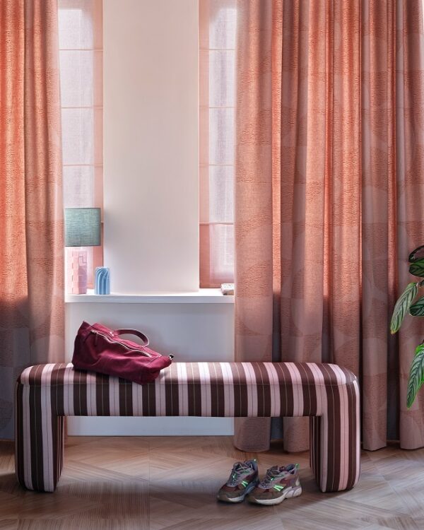 Woonkamer met houten vloer, bankje, kamerhoge overgordijnen en vouwgordijnen.