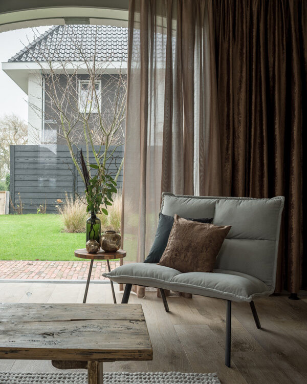 Woonkamer met transparante vitrages, gecombineerd met dikke, verduisterende overgordijnen die halfopen zijn, met zicht op een tuin in de achtergrond