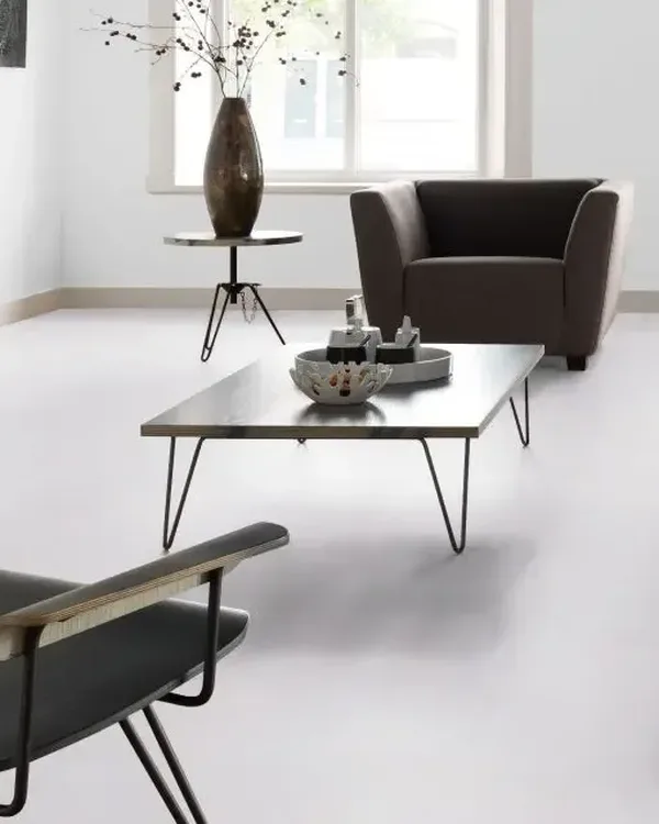 Lichte woonkamer met lichtgrijze marmoleumvloer, bruine fauteuil, lage salontafel en witte schouw