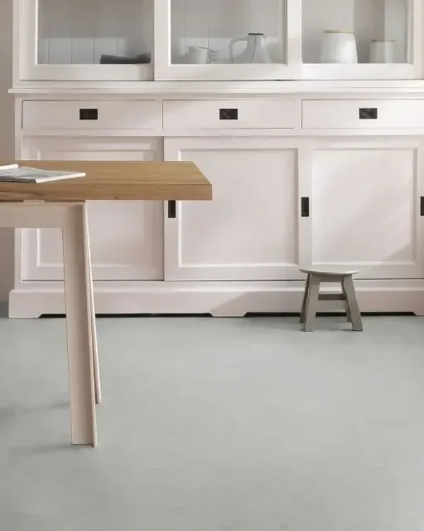 Keuken met lichtgrijze marmoleumvloer, witte buffetkast en houten eettafel