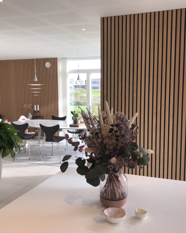 Open keuken met houten akoestische wandpanelen en eettafel met warme accenten.