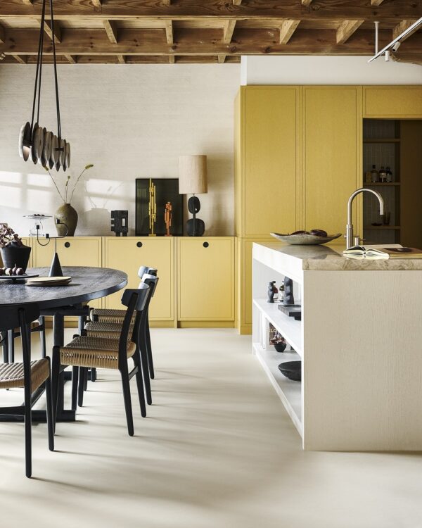 Woonkeuken met houten keukenkasten, zwarte eettafel en stoelen en lichtgrijs kookeiland met lichtgrijze marmoleum vloer.