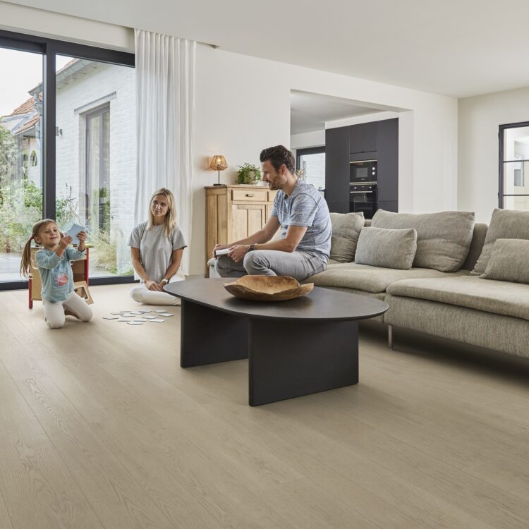 Woonkamer met houtlook pvc vloer en vloerverwarming, ouders en kind zitten op de grond een spelletje te spelen.