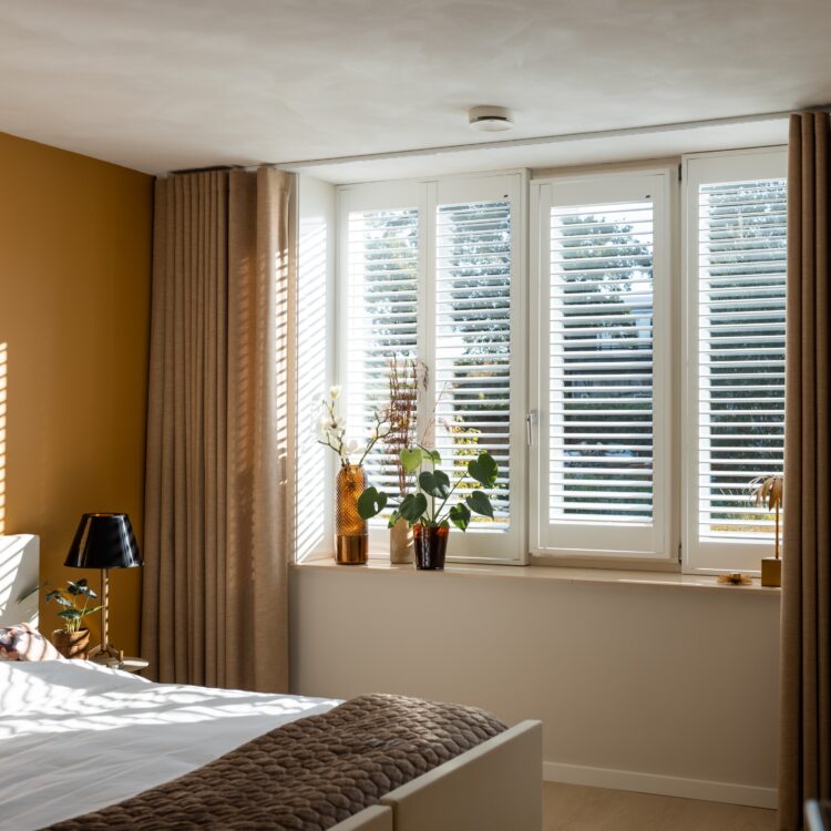 Gezellige slaapkamer met witte houten shutters en kamerhoge overgordijnen.