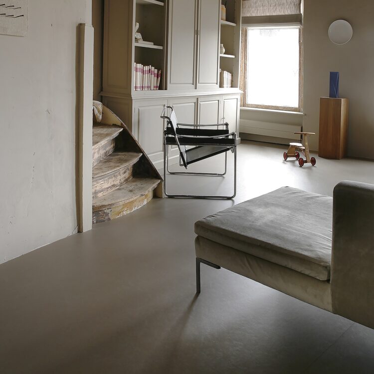 Woonkamer in neutrale kleuren met grote houten kast, bank en bruingrijze marmoleum vloer.