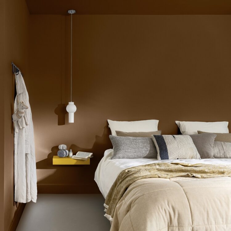 Slaapkamer in warme bruintinten met geel kleuraccent en bed met zachte kussens en linnen sprei.