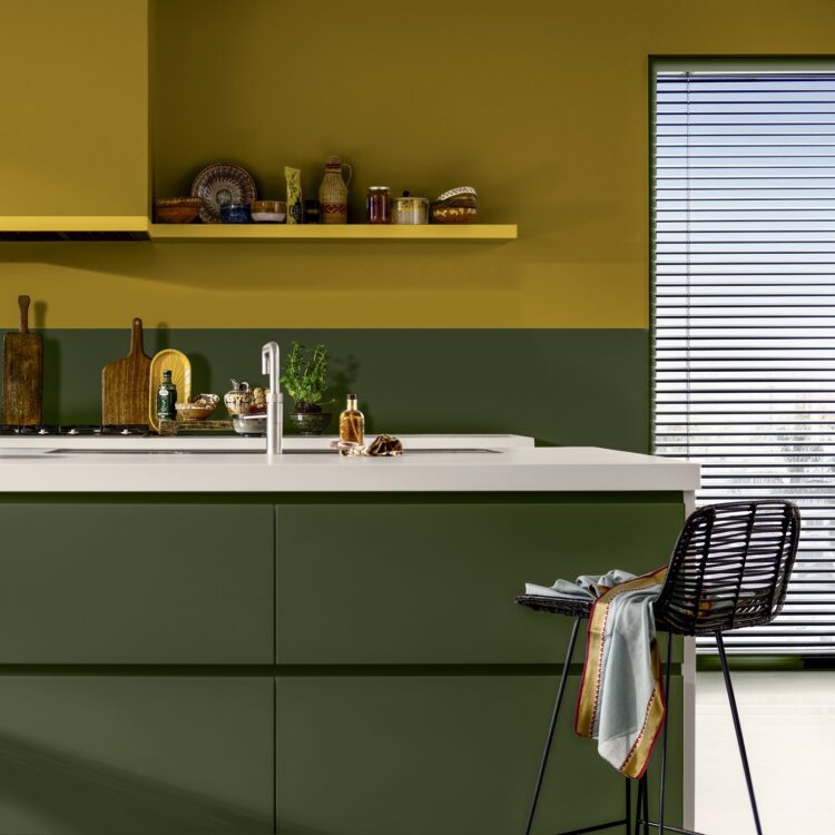 Keuken in Italiaanse stijl met muur in True Joy geel, mosgroene keukenkastjes en aardewerk kruidenpotjes als accessoires.