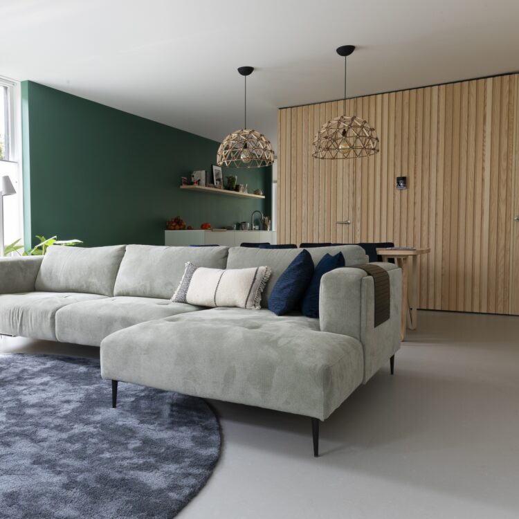 Woonkamer met lichtgrijze marmoleum vloer, lichtgrijze hoekbank en wandpanelen in eikenhout look.