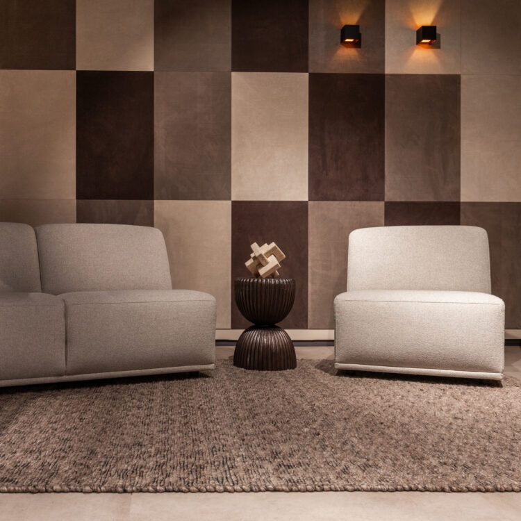 Woonkamer met leren wandbekleding van Belledo in bruin en beige tinten met grijze 2 zits en fauteuil.