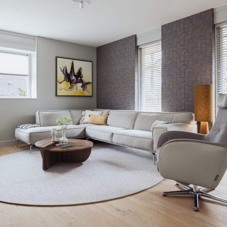 Woonkamer met houtlook pvc vloer, lichtgrijze hoekbank en fauteuil