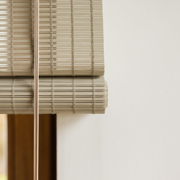 Close-up van geweven rolgordijnmateriaal, natuurlijk hout en warme textuur zichtbaar.