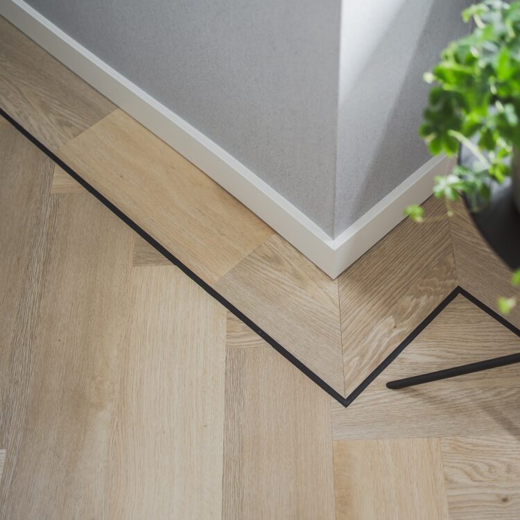 Detail witte plint langs houten visgraat pvc vloer.