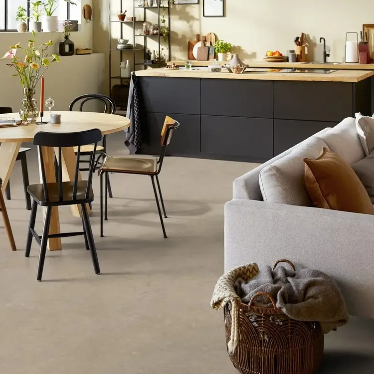 Open woonkeuken met taupekleurige marmoleumvloer, ronde houten eettafel, lichte bank en zwart keukeneiland