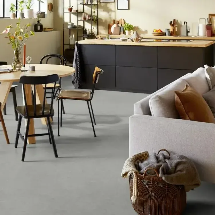 Open woonkeuken met lichtgrijze marmoleumvloer, ronde houten eettafel met zwarte stoelen en een lichte bank