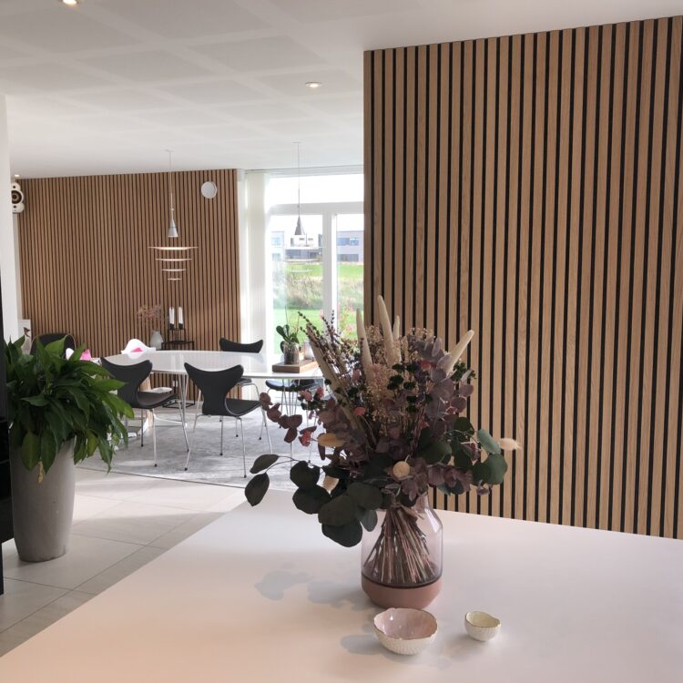 Open keuken met houten akoestische wandpanelen en eettafel met warme accenten.