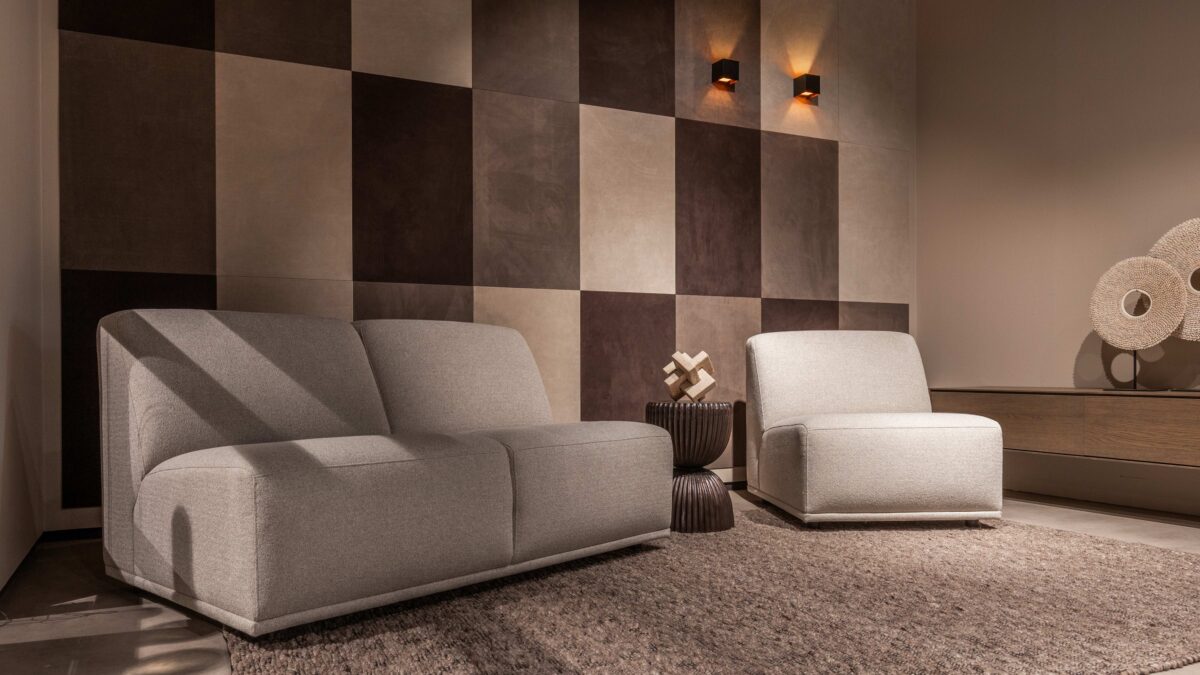 Woonkamer met leren wandbekleding van Belledo in bruin en beige tinten met grijze 2 zits en fauteuil.